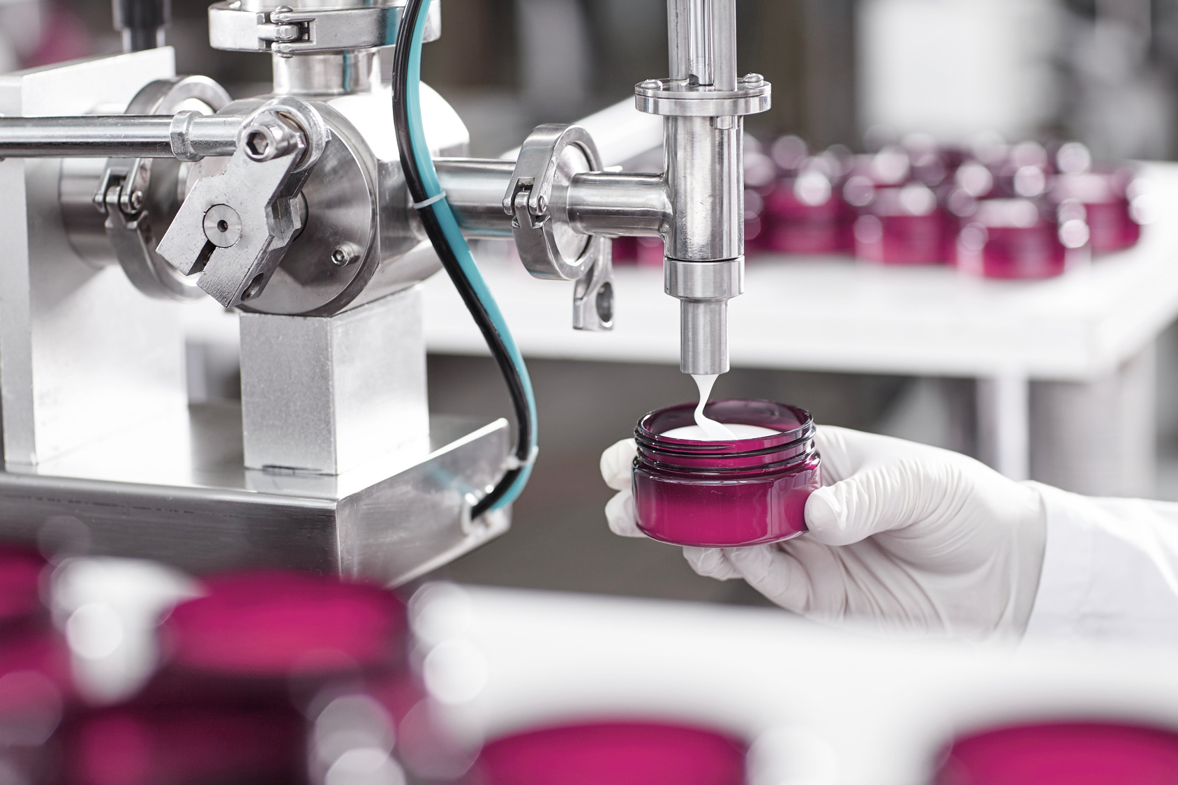 Production and packaging of cosmetics products. Cropped shot of factory worker in gloves and gown holding plastic jar, filling it with white face or body cream. Beauty, skincare and cosmetology